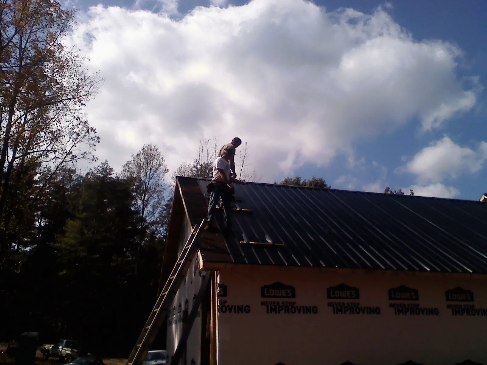 Roofer fastening dark metal panels high against a cloudy sky, from a Roof Inspection job in Curtis Bay