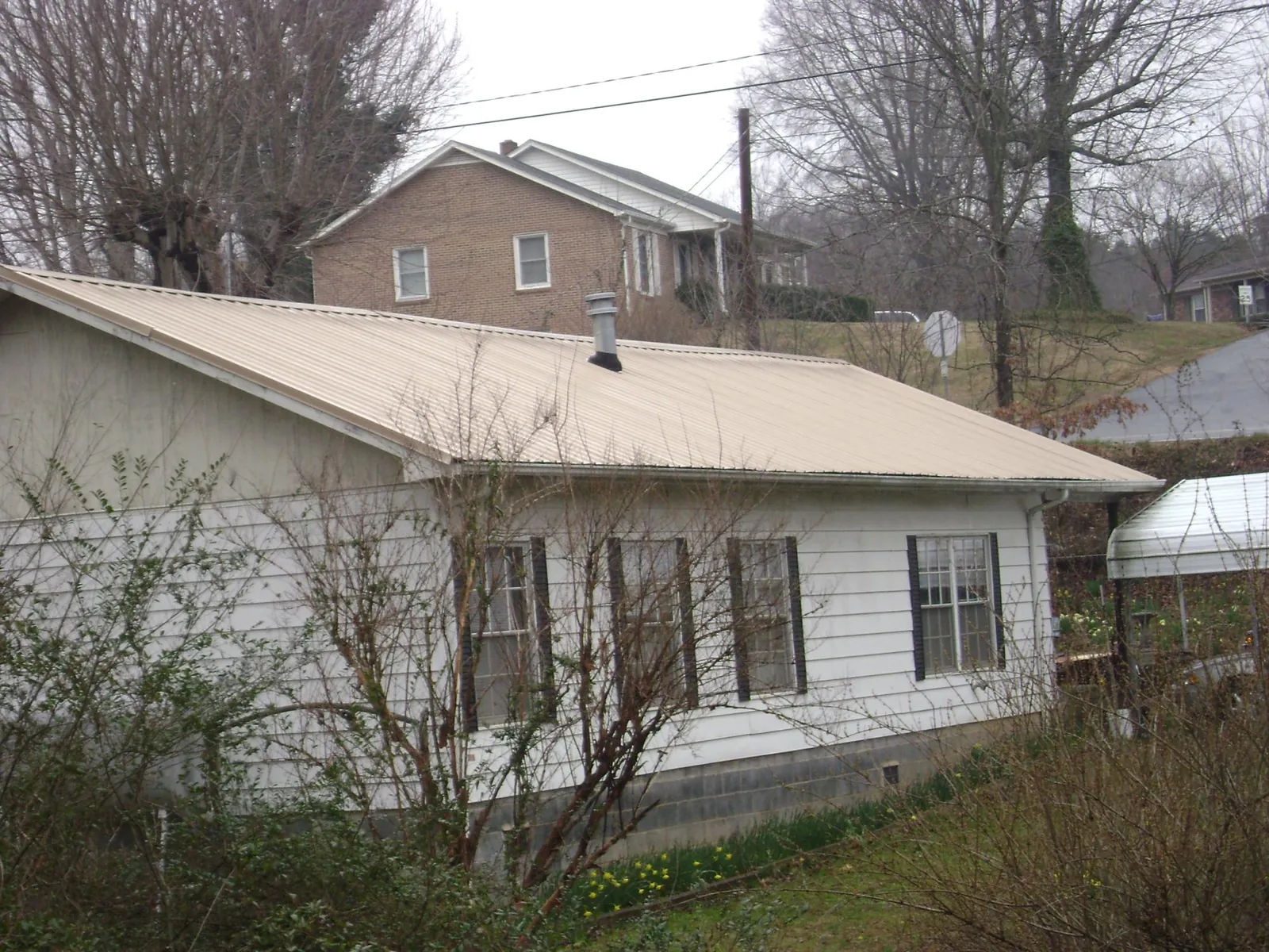 Tan metal roof on a white sided house set into a hillside — Commercial Roofing by Roofing Brothers in Curtis Bay